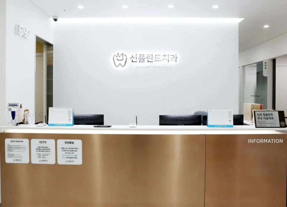 벽에 선플란트치과 로고가 붙은 흰 벽 앞의 접수대